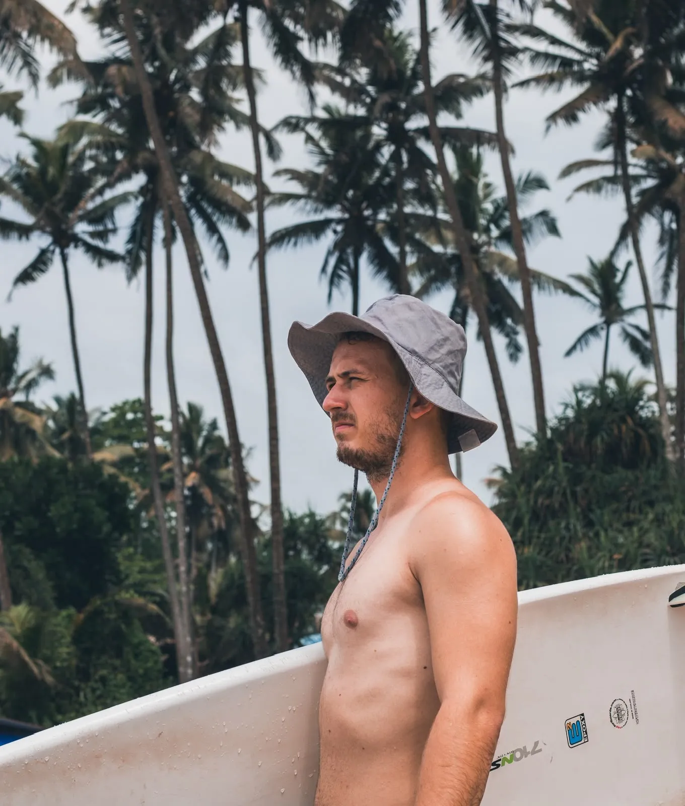 Portrait of a surfer with his board under the palm trees