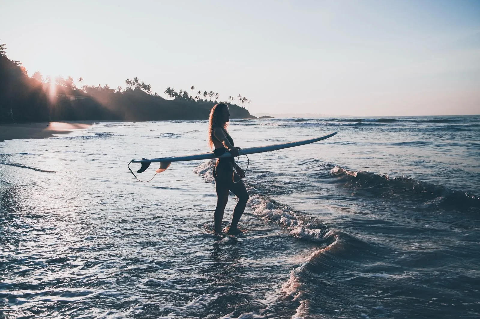 Surfer standing in the shallows against the low sun