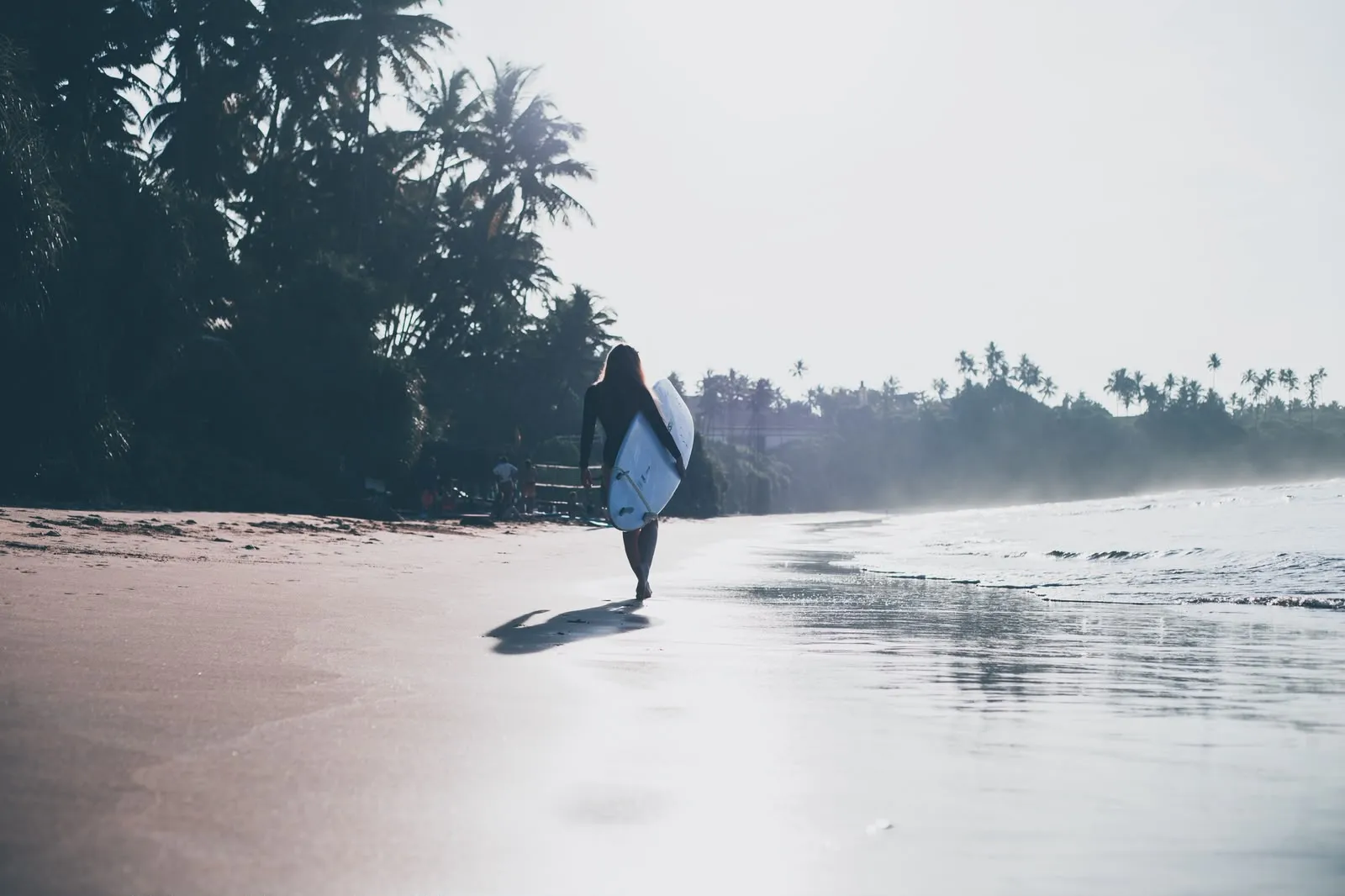 Surfer walking along the shoreline in backlight